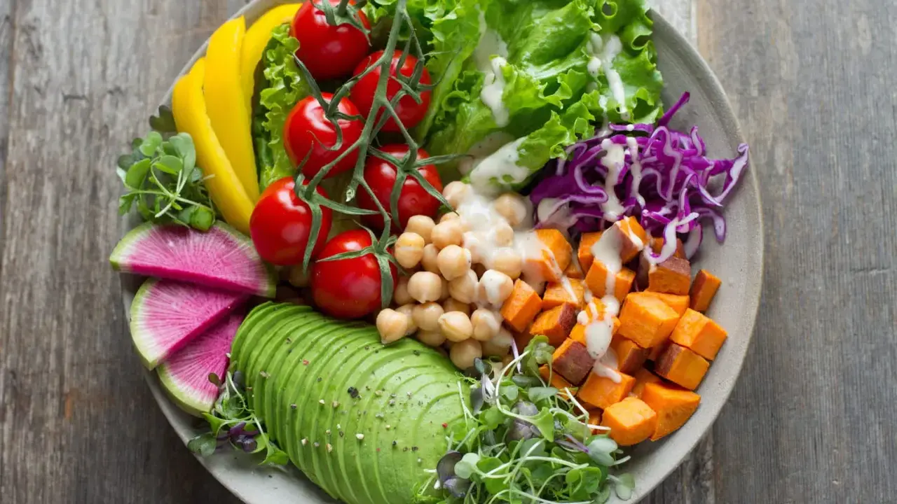 Un bol coloré avec avocat, tomates, pois chiches, patates douces, chou rouge, radis et poivron jaune. Parfaites salades originales pour buffet.