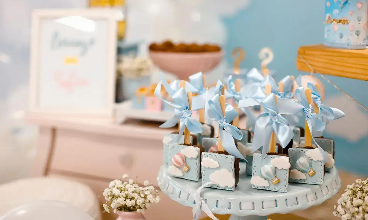 Garniture de table pour baby shower avec des chocolats décorés de montgolfières bleues et de nuages.