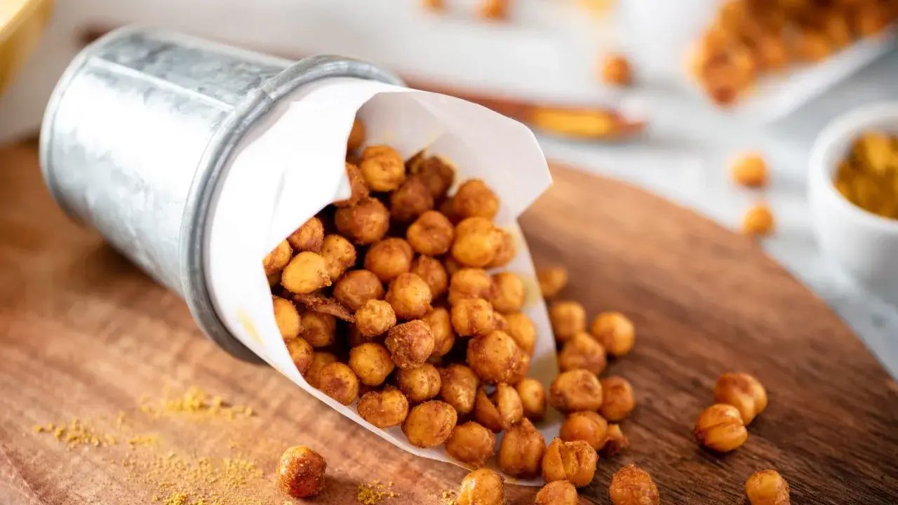 Un seau renversé déverse des pois chiches rôtis, parfaits pour des snacks sains. Une pincée d'épices dorées parsème le bois.