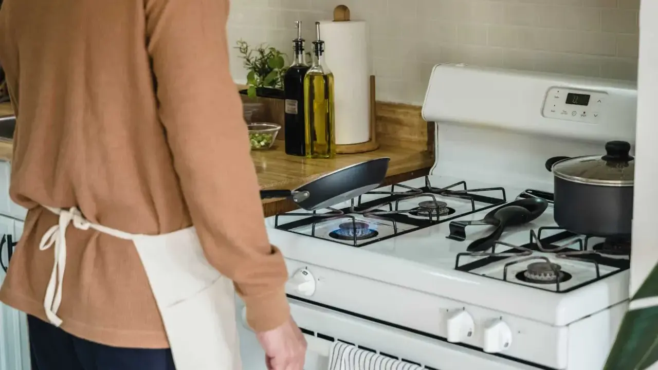 Un homme en tablier prépare à nettoyer graisse brûlée gazinière. Une poêle chauffe sur le feu.