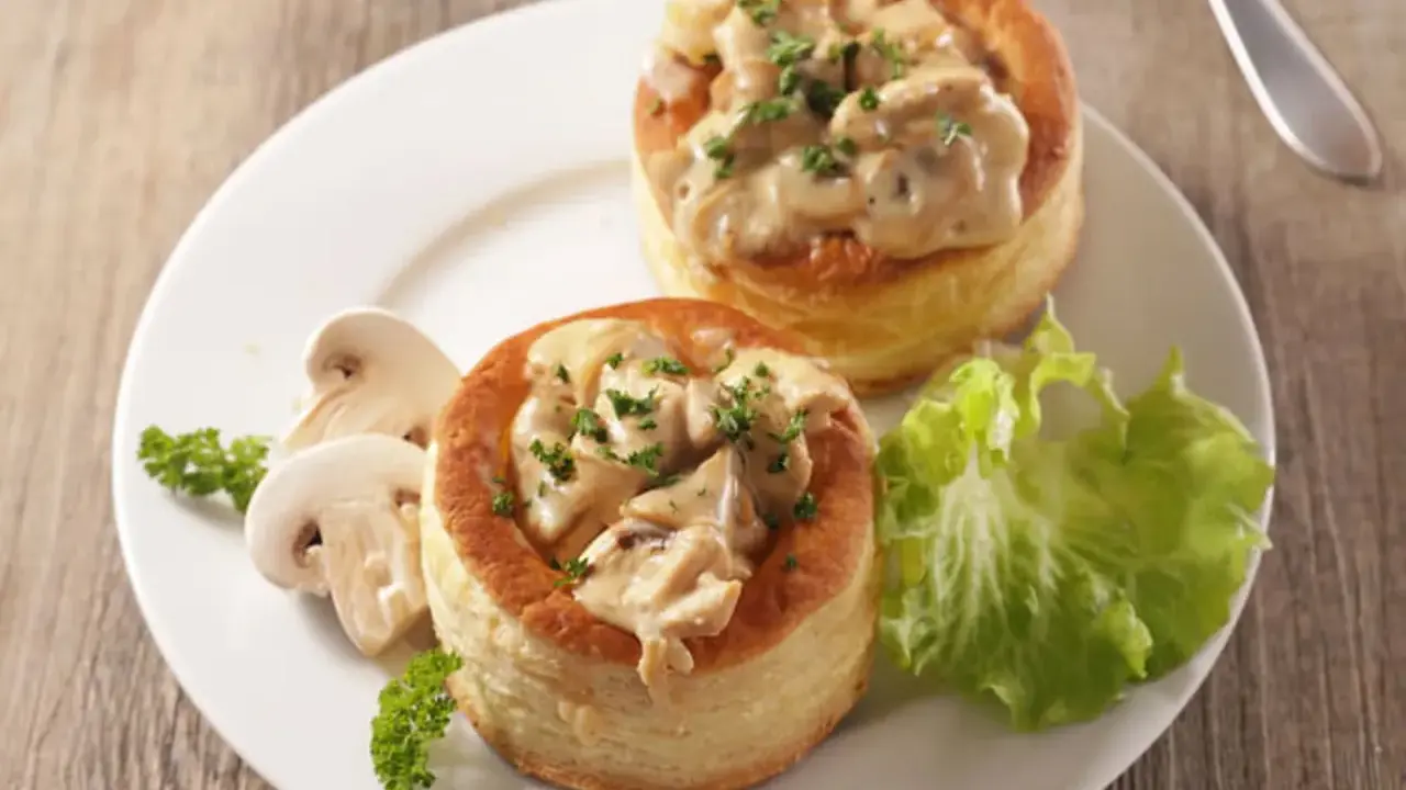 Deux bouchées à la reine maison, garnies d'une sauce crémeuse aux champignons et persil, servies avec des champignons frais et une feuille de laitue.