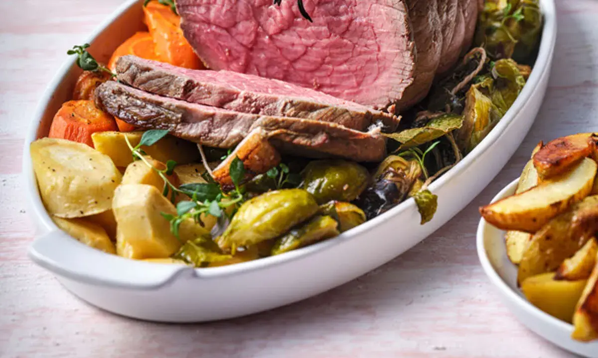 Tranches de rosbeef froid, accompagnées de pommes de terre rôties, carottes et choux de Bruxelles dans un plat blanc.
