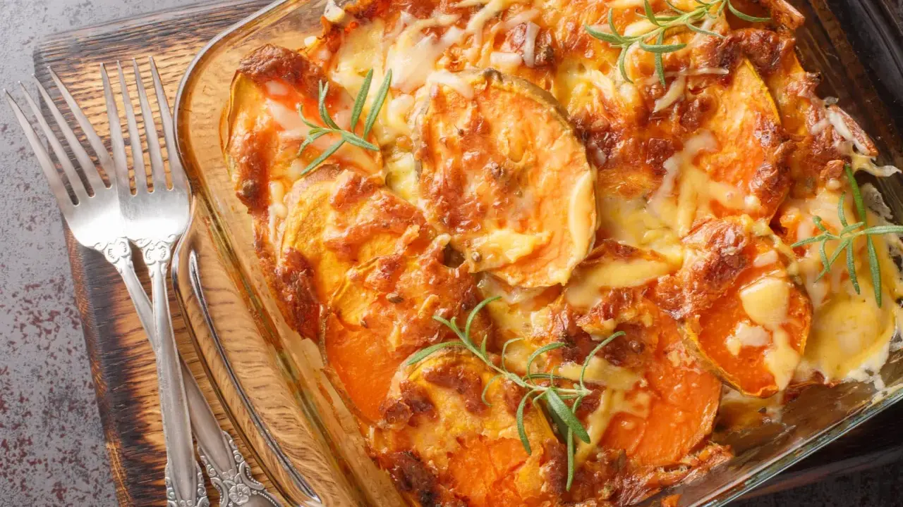 Gratin de patates douces au fromage, prêt pour un repas d'anniversaire. Deux fourchettes argentées sont posées sur le côté.