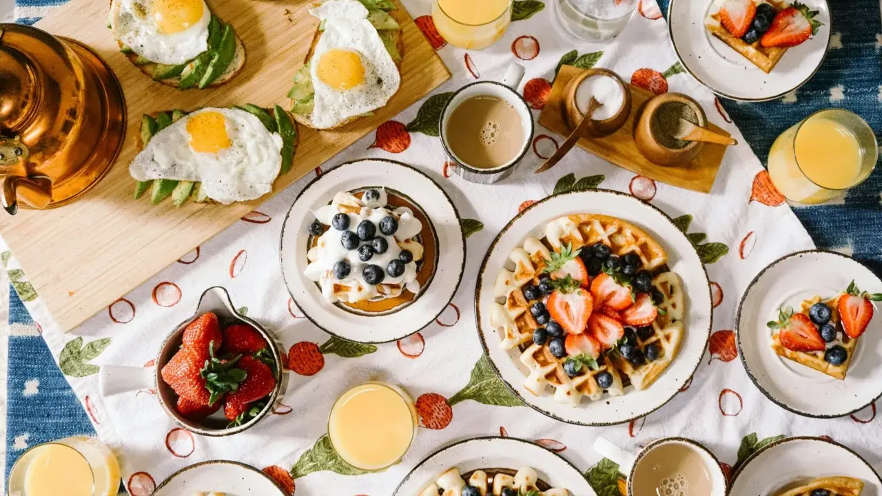 Un petit déjeuner continental ou américain avec des toasts à l'avocat et aux œufs, des gaufres aux fruits rouges et des jus.