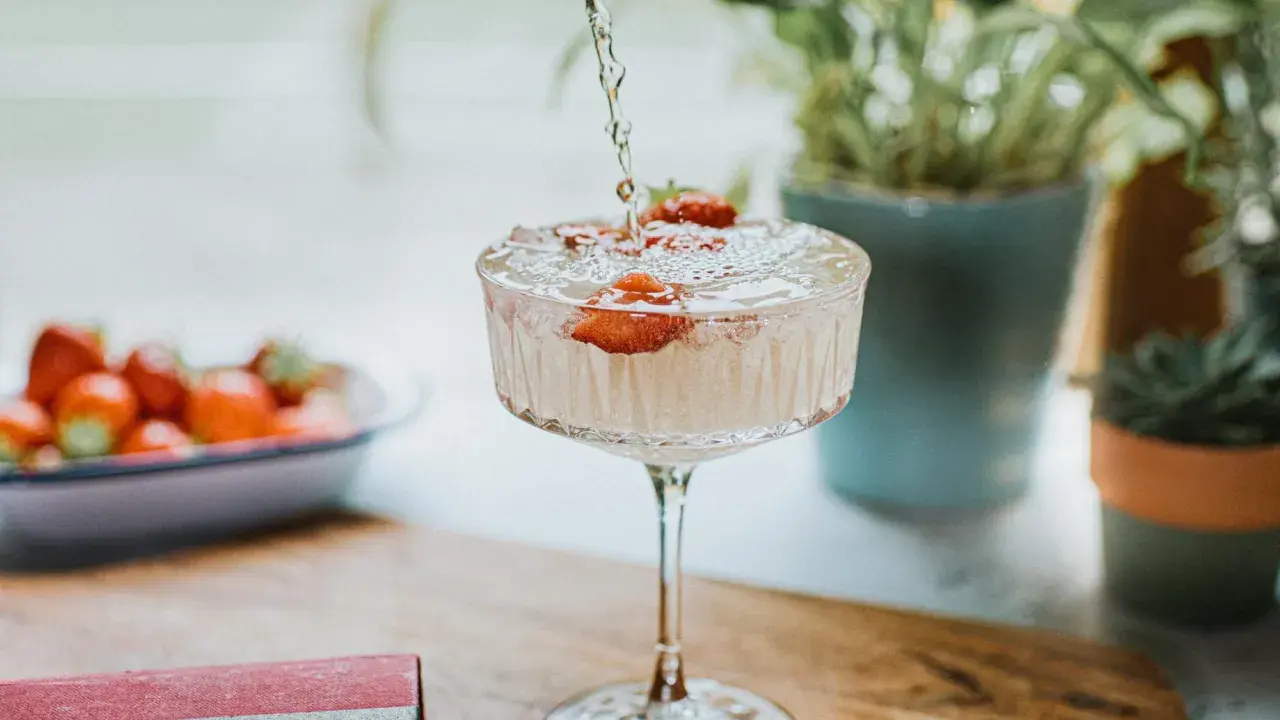 Un cocktail sans alcool surprenant, avec des fraises fraîches, est préparé. Des plantes vertes en arrière-plan ajoutent une touche de nature.