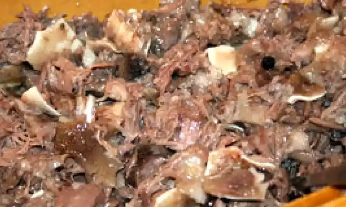 Un plat de fromage de tête, avec des morceaux de viande et de cartilage, dans un récipient en bois.