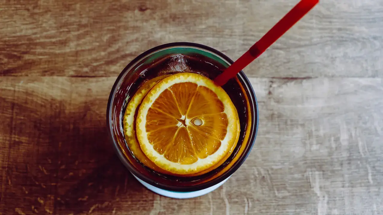 Verre de boisson sans alcool pour accompagner repas, avec rondelles d'orange et glaçons, sur fond de bois.