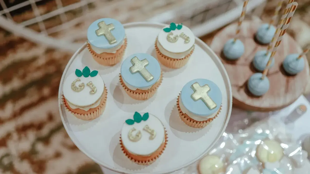 Jolis cupcakes décorés de croix dorées et de lettres pour un buffet dessert baptême. Des cake pops bleus sont aussi présents.