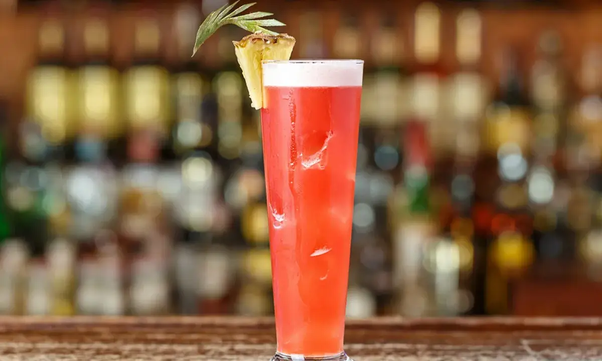 Un cocktail rouge vif, garni d'ananas, sur un bar. Idéal pour un cocktail pas cher pour 10 personnes, facile à préparer.
