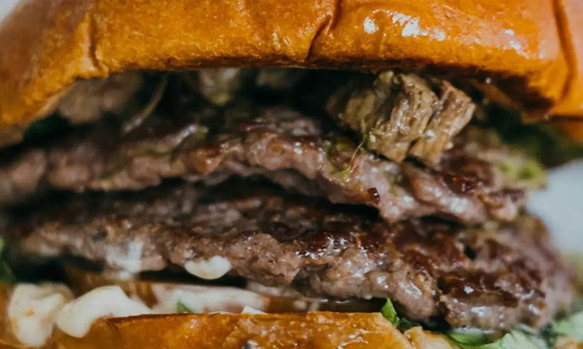 Gros plan sur un steak burger double, avec des steaks juteux, de la sauce et de la laitue entre deux pains briochés dorés.