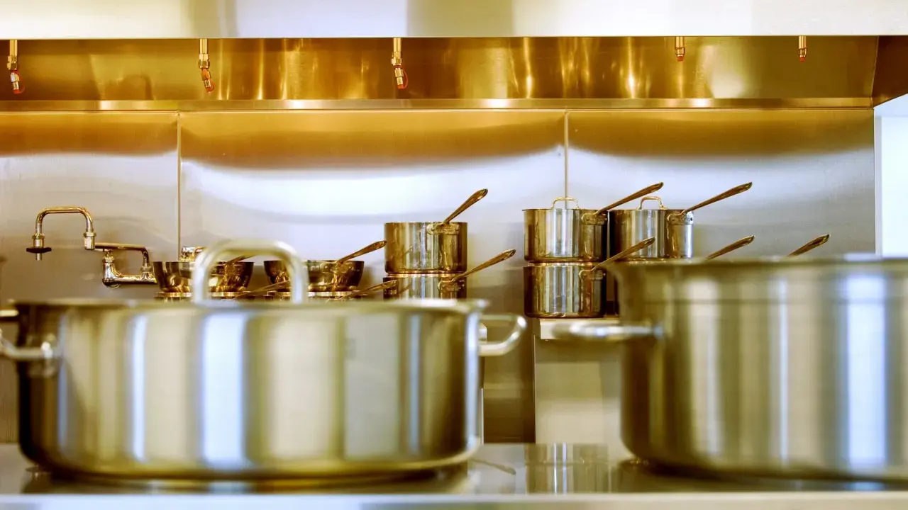 Une cuisine professionnelle avec des casseroles en acier inox 18/10 étincelantes. Des robinets chromés et des gicleurs de sécurité complètent l'ensemble.
