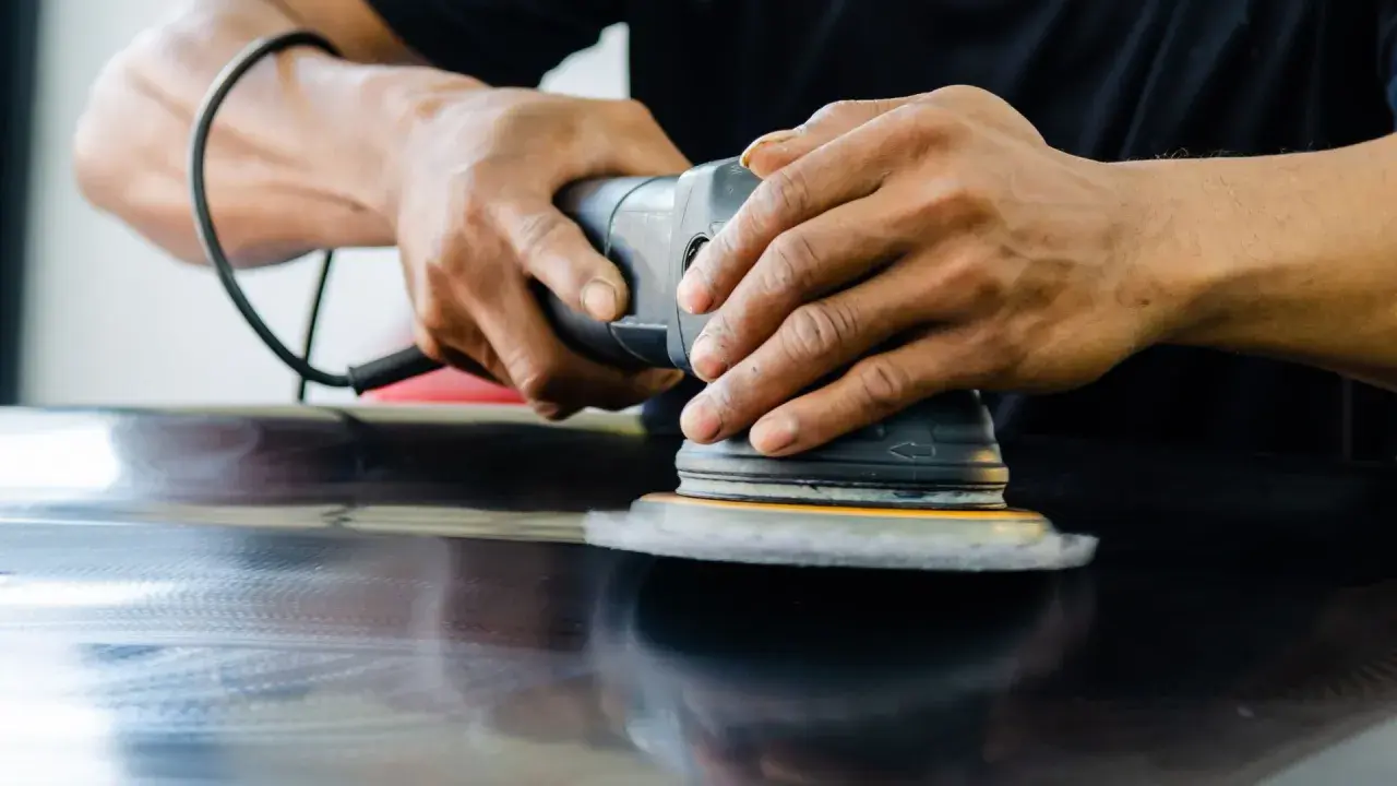 Mains polissant une surface sombre avec une ponceuse orbitale pour polir aluminium rayé.