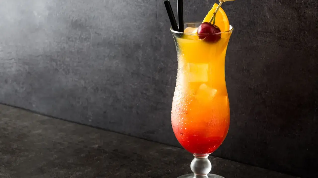 Cocktail Sex on the Beach recette 5l, dégradé rouge-orange, garni d'une cerise et d'une tranche d'orange.
