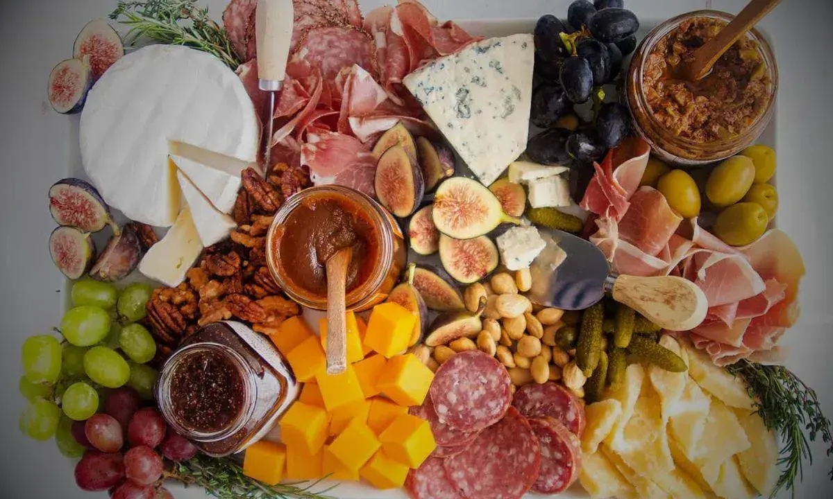 Plateau charcuterie et fromages : un buffet généreux avec jambon, saucisson, fromages variés, fruits, noix et confitures.