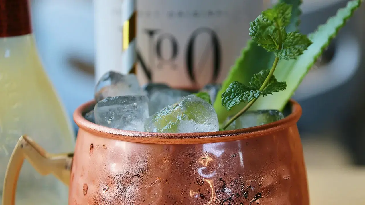 Un Moscow Mule rafraîchissant dans sa tasse en cuivre, garni de menthe et d'une tranche d'agrume.
