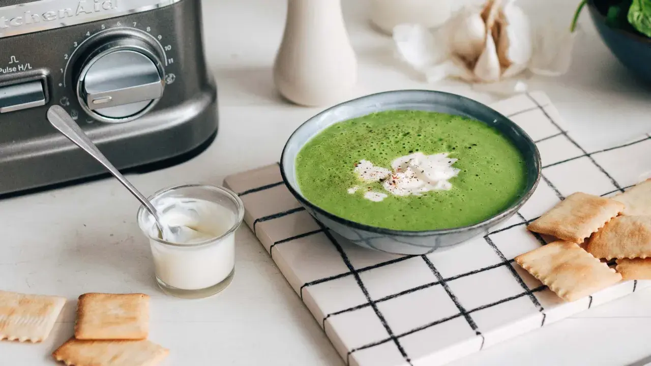 Une délicieuse soupe de légumes variés, onctueuse et verte, garnie de crème et servie avec des crackers.