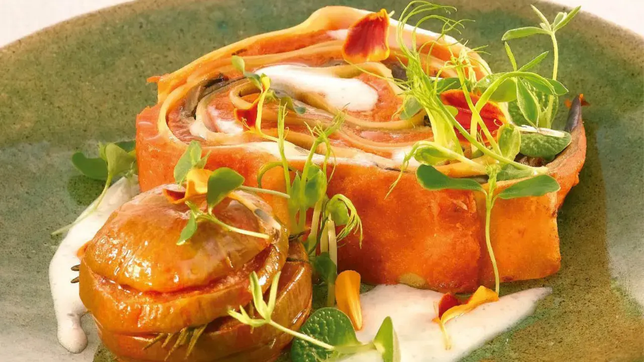 Un roulé de pâtes orange, garni de crème et de pousses, avec une petite boule caramélisée. Un plat qui rappelle les "maccheroni della mamma".