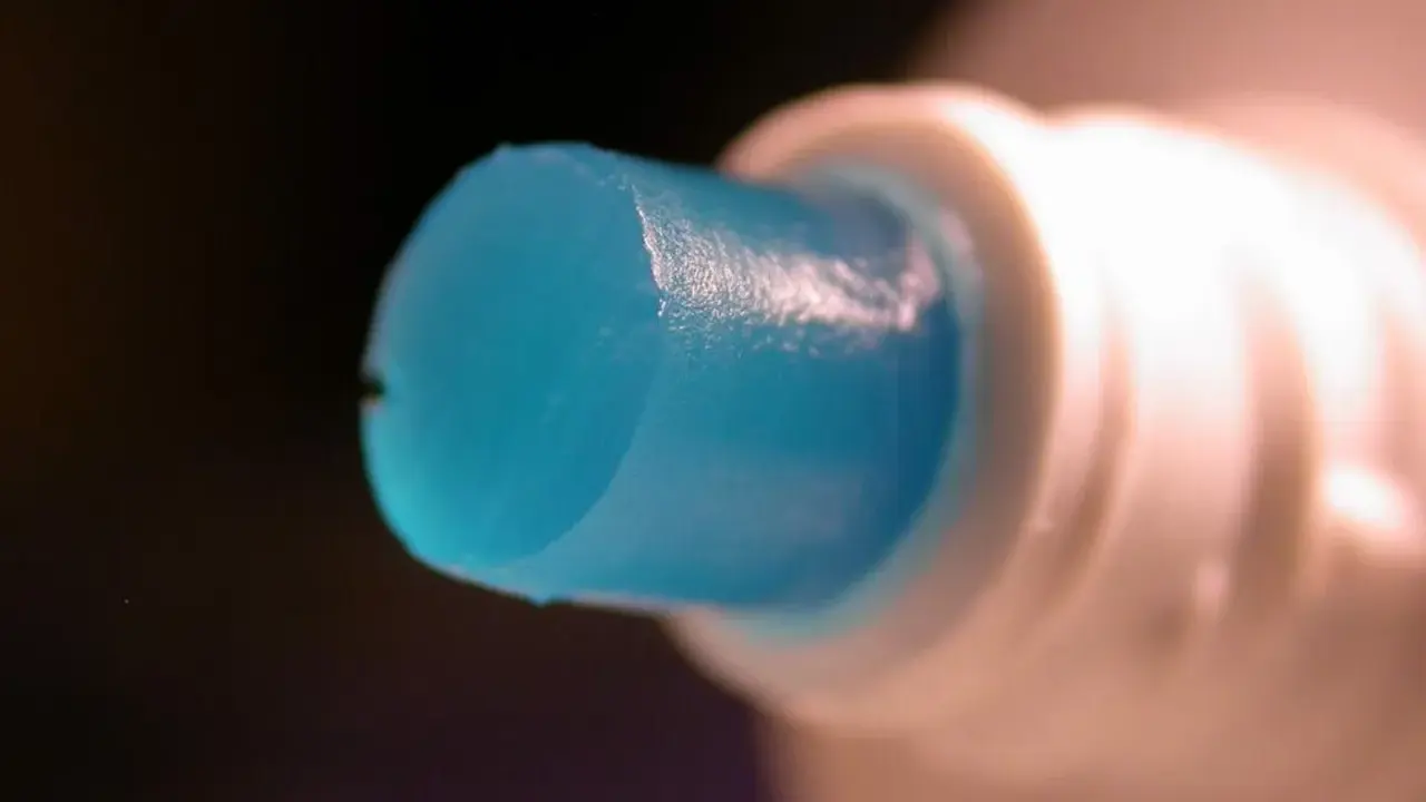 Goutte de dentifrice bleu sortant d'un tube blanc, parfaite pour polir l'aluminium.