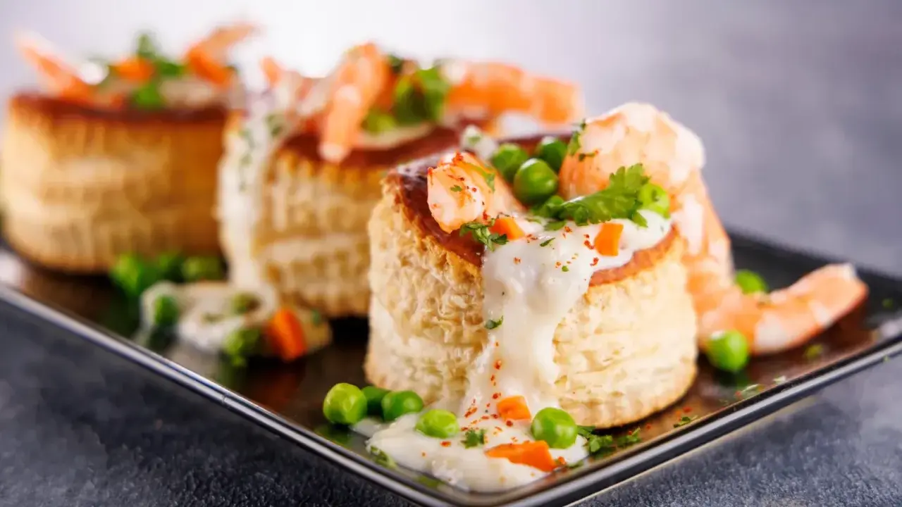 Trois bouchées de tapas crevette, garnies de crevettes, petits pois et sauce crémeuse, sur un plateau noir.