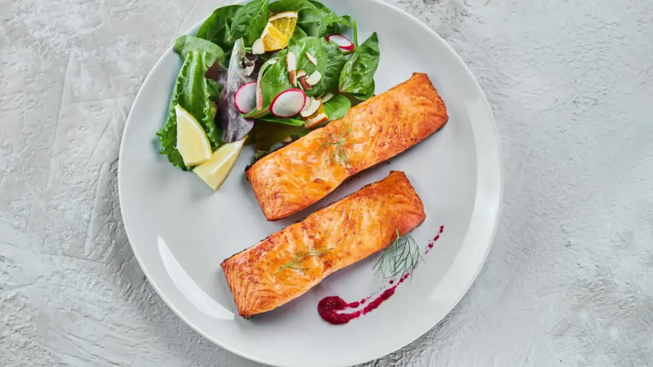 Deux pavés de saumon au four, accompagnés d'une salade fraîche et de quartiers de citron. Un délice simple et savoureux.