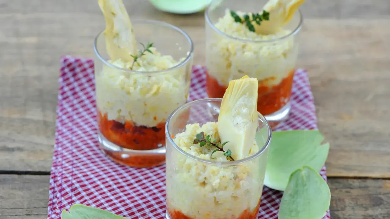 Trois verrines artichaut, garnies d'une purée crémeuse et d'une touche de sauce tomate, sur un fond de bois rustique.