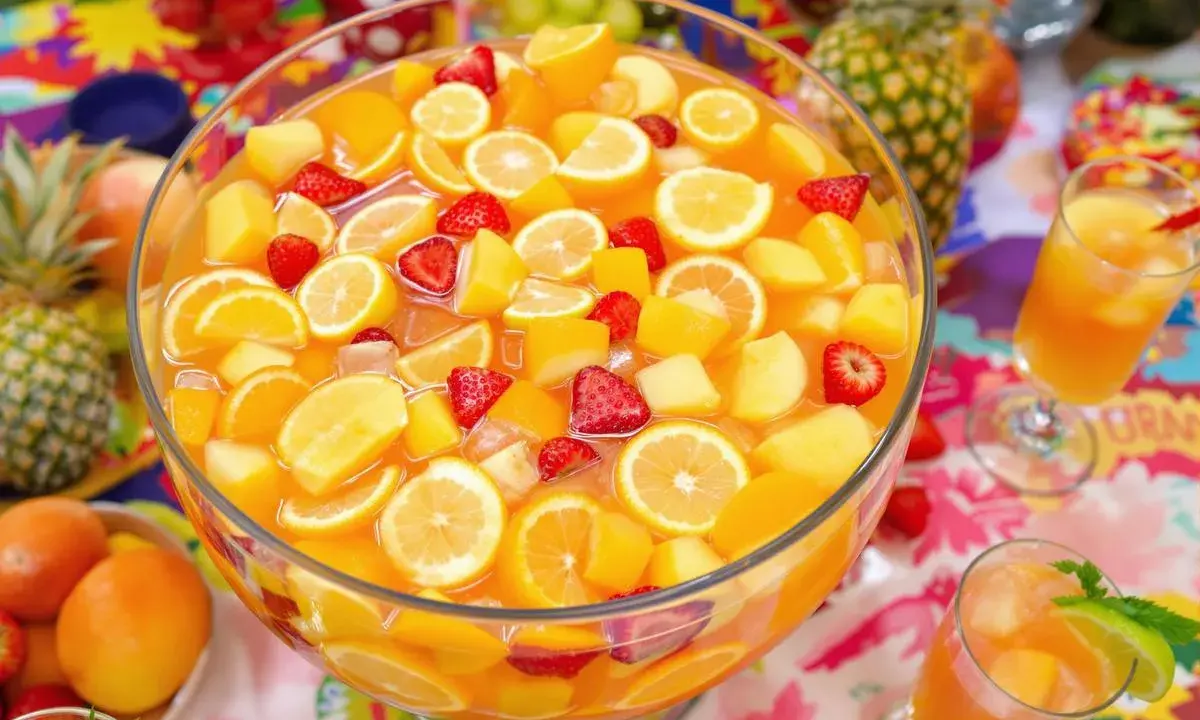Un grand bol de punch aux fruits colorés, parfait pour une recette de punch sans alcool pour 30 personnes. Fraises, oranges, citrons et morceaux de pêche flottent dans un liquide orangé.