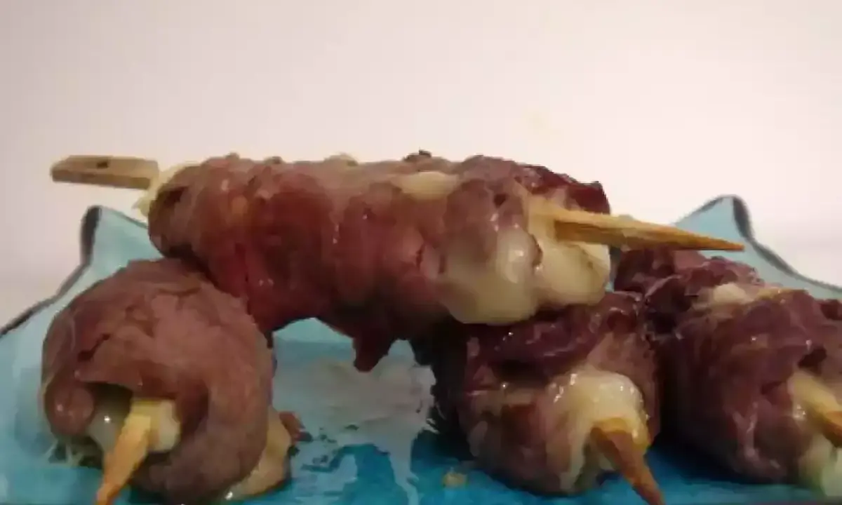 Brochettes de boeuf roulées autour de fromage fondant, servies sur une assiette bleue.