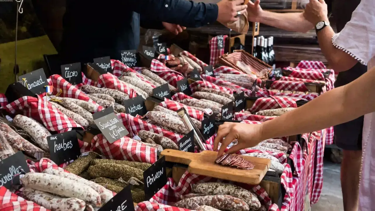 Vitrine de charcuterie avec de nombreuses saucisses et un client qui en choisit une tranche.