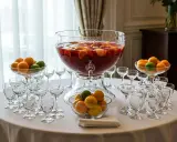 Un grand punch Lafayette débordant de fruits, entouré de verres et de bols d'oranges et de citrons verts, prêt pour une fête.