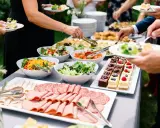 Un buffet garni pour un plat soiree : salades fraîches, charcuteries, et petits gâteaux décorés. Les invités se servent.