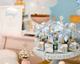 Garniture de table pour baby shower avec des chocolats décorés de montgolfières bleues et de nuages.