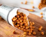 Un seau renversé déverse des pois chiches rôtis, parfaits pour des snacks sains. Une pincée d'épices dorées parsème le bois.