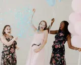 Trois femmes célèbrent un gender reveal, avec des confettis bleus et des ballons roses et bleus. C'est quoi ce moment joyeux !