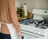 Un homme en tablier prépare à nettoyer graisse brûlée gazinière. Une poêle chauffe sur le feu.