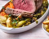 Tranches de rosbeef froid, accompagnées de pommes de terre rôties, carottes et choux de Bruxelles dans un plat blanc.