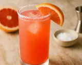 Un verre de Paloma, cocktail rose vif, garni d'une tranche de pamplemousse et de sel. La recette est simple et rafraîchissante.