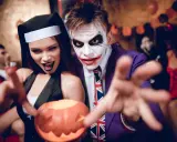 Un couple en costumes effrayants, une nonne et le Joker, profite d'une **soirée costumée** d'Halloween, tenant une citrouille sculptée.