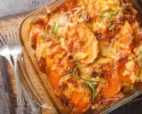Gratin de patates douces au fromage, prêt pour un repas d'anniversaire. Deux fourchettes argentées sont posées sur le côté.