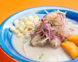 Ceviche frais baignant dans un leche de tigre crémeux, garni d'oignons rouges, de coriandre, de maïs et de patate douce.