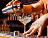 Un barman verse un liquide d'un shaker dans un verre à cocktail rempli de glace. Les shakers sont essentiels pour créer des boissons rafraîchissantes.