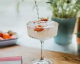 Un cocktail sans alcool surprenant, avec des fraises fraîches, est préparé. Des plantes vertes en arrière-plan ajoutent une touche de nature.