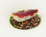 Un poisson blanc délicat, garni de fines lamelles de betterave rouge, repose sur un lit de grains de riz noir et de morceaux de poulpe, le tout nappé d'une sauce verte vibrante. Une œuvre d'art culinaire, un de ces mets d'exception.