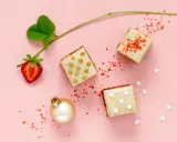 Délicieux petits fours sucrés, parfaits pour une recette de fête. Une fraise, une boule de Noël et des paillettes rouges complètent la scène.