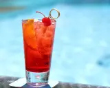 Un cocktail sans alcool à préparer la veille, garni d'une cerise et d'une tranche d'orange, prêt à être dégusté au bord de la piscine.