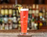 Un cocktail rouge vif, garni d'ananas, sur un bar. Idéal pour un cocktail pas cher pour 10 personnes, facile à préparer.