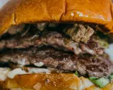 Gros plan sur un steak burger double, avec des steaks juteux, de la sauce et de la laitue entre deux pains briochés dorés.