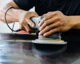 Mains polissant une surface sombre avec une ponceuse orbitale pour polir aluminium rayé.