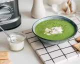 Une délicieuse soupe de légumes variés, onctueuse et verte, garnie de crème et servie avec des crackers.