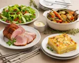 Un rôti de porc froid tranché, servi avec une salade verte croquante, des légumes rôtis, un gratin et une sauce crémeuse. Parfait pour un repas d'été.