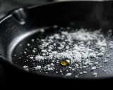 Goutte d'huile dorée sur une **casserole noircie** saupoudrée de sel. Prête pour une cuisson savoureuse.